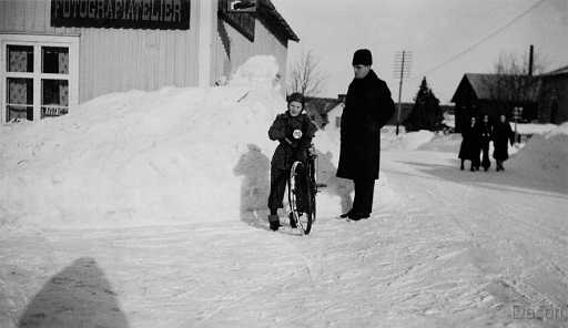 1940 Knut och Uno utanför fotoatelie.jpg - Foto från 1940 sonen Uno med cykel övervakas av fader Knut till vänster fotoateljén och till höger syns Odal Näsbergs cykelverkstad, på gaveln hade Hjalmar Berg en liten affär.
